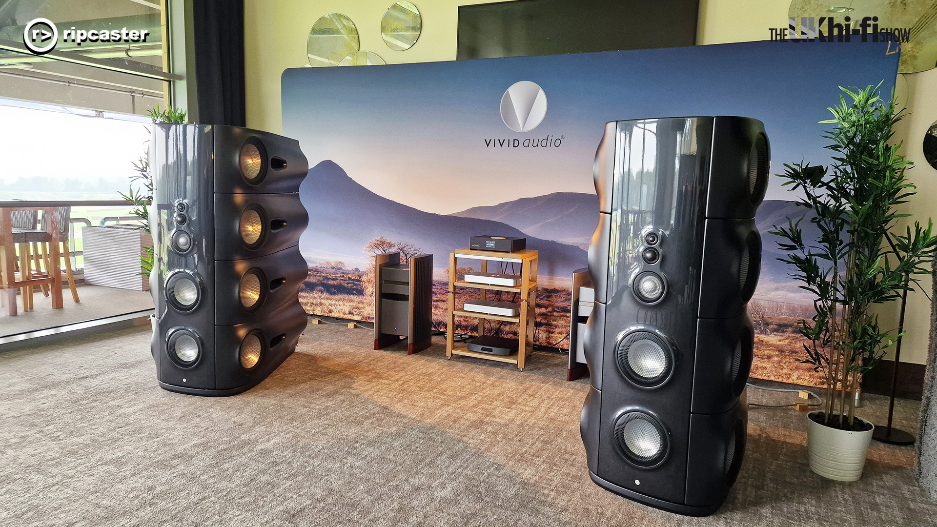 Vivid Audio.  Two large, black, floorstanding speakers either side of some hifi equipment on a stand.  