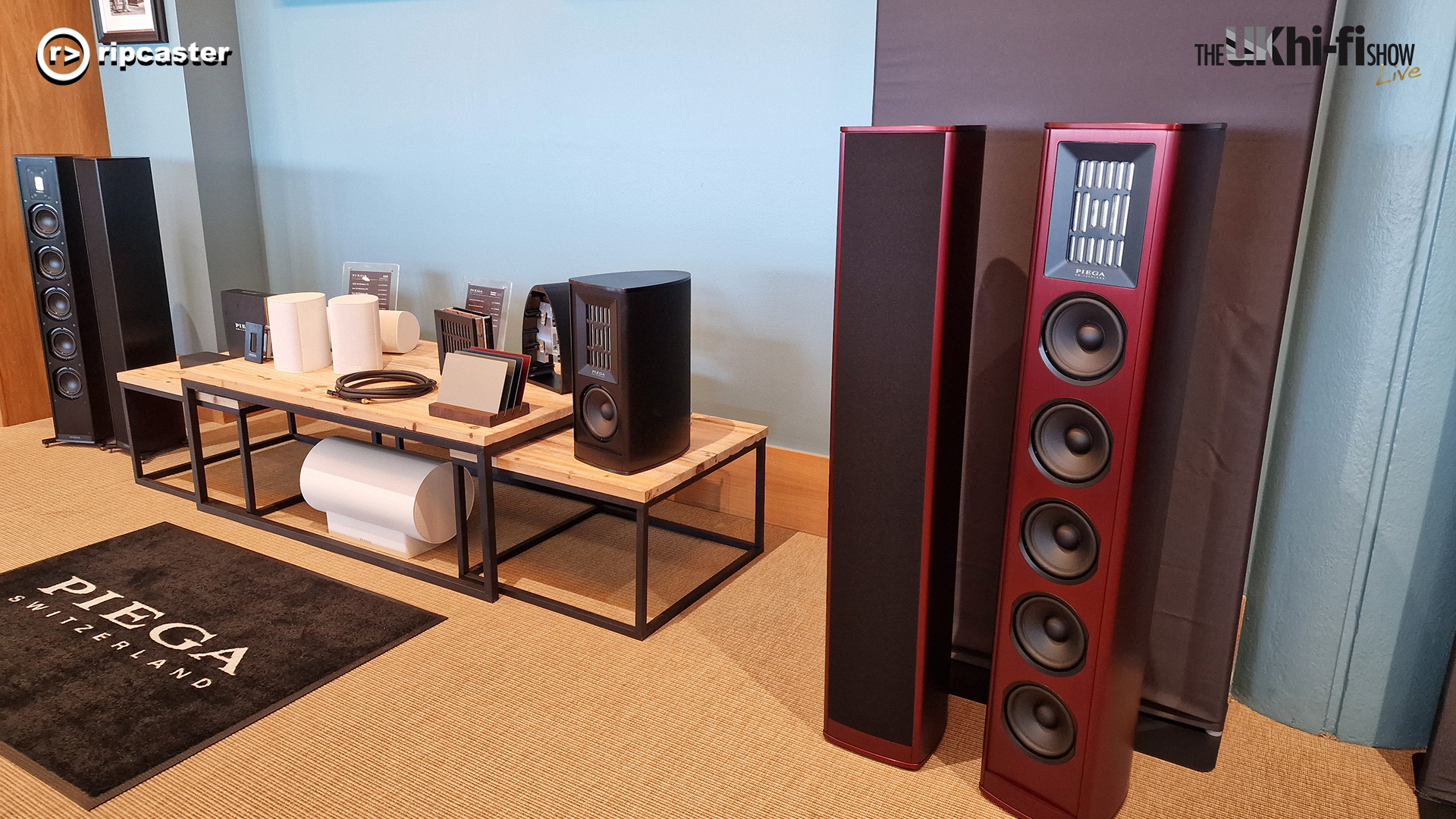 Piega.  Two pairs of floorstanding speakers either side of smaller speakers on a table 