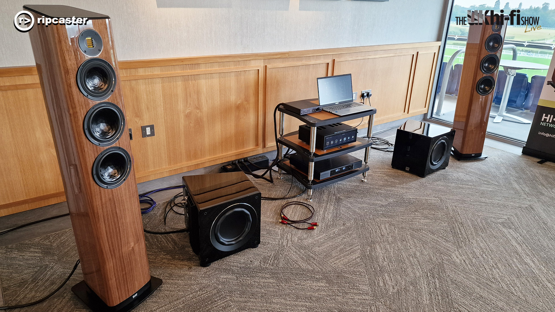 A pair of wooden floorstanding speakers with subwoofers and HiFi equipment at the Ascot 2024 Show