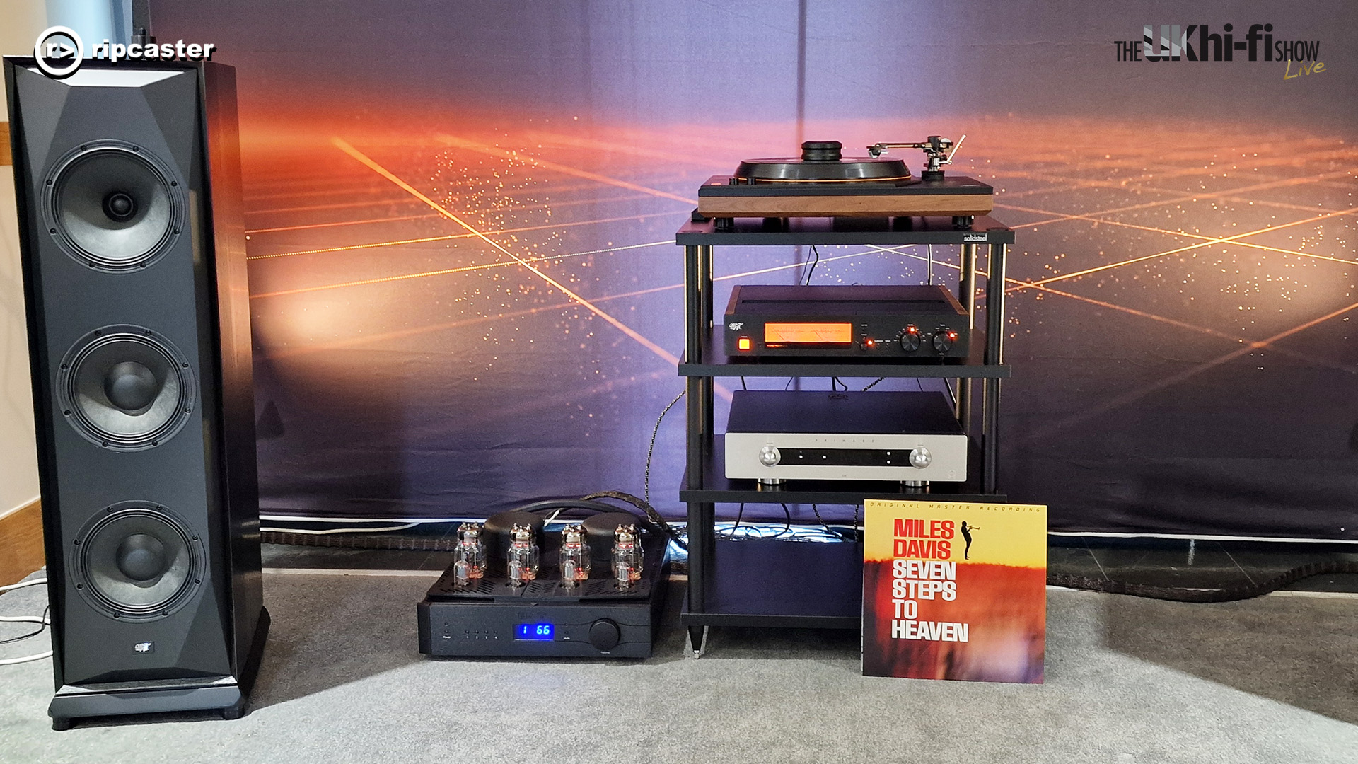 A black floorstanding speaker beside a stack of HiFi equipment