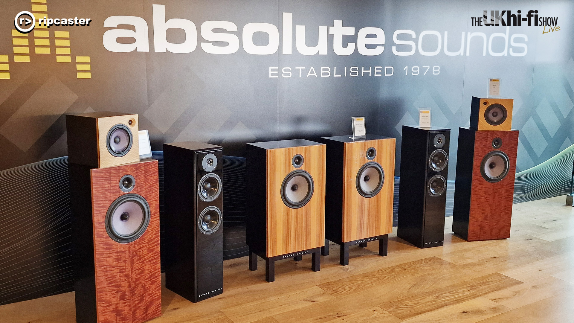 A selection of speakers lined up in front of a backdrop that says "absolute sounds"