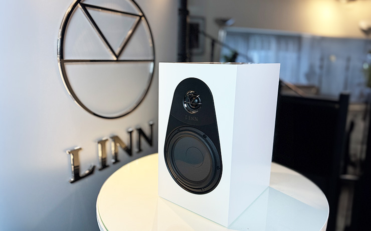 The Linn 119 speaker in white beside the ripcaster Linn sign.  The speaker is on a white circular table