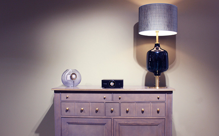 The Cabasse AMP 240 S on top of a wooden unit with a lamp one side and a vase the other.