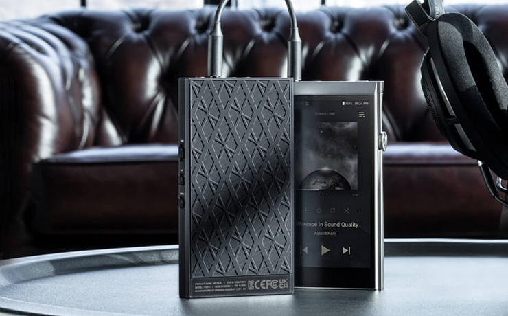 Astell & Kern AKPA10 Portable Class-A Amplifier connected to an A&K player on a table with a sofa in the background
