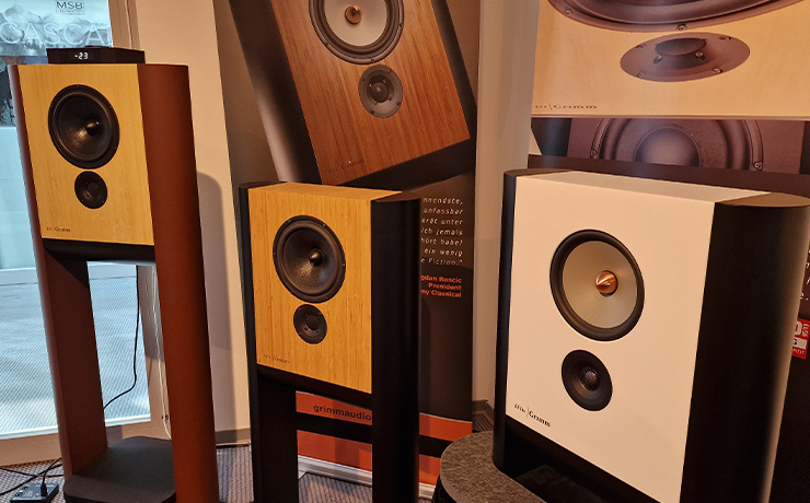 Grimm loudspeakers with the LS1be in white in the bottom right of the image.  there are two other Grimm speakers to the left of the image