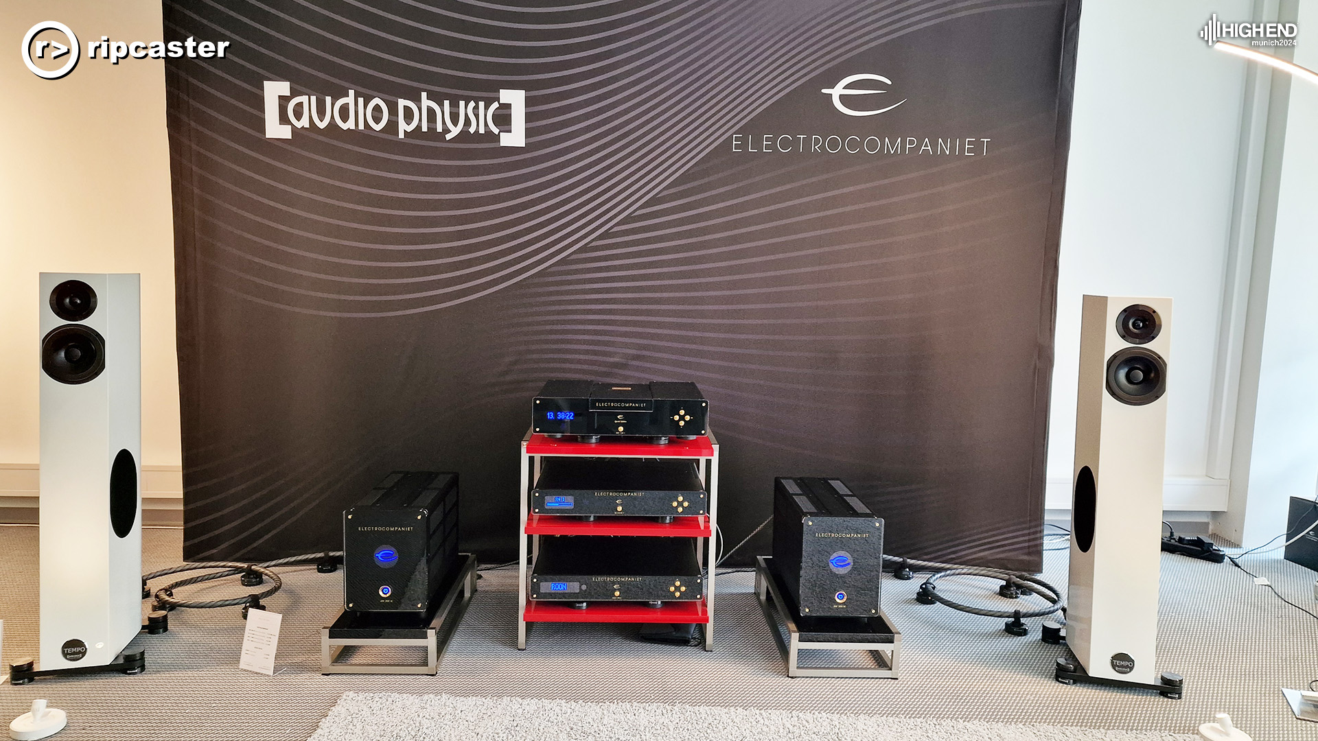 a pair of white floorstanding speakers either side of some other HiFi equipment on a red HiFi unit