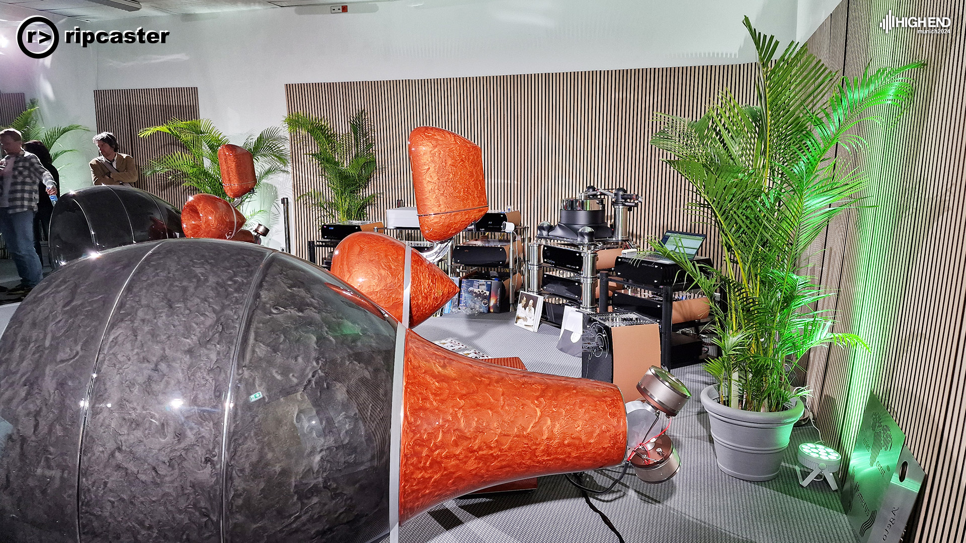 A side view of the racing car tyres speakers.  they are orange and dark grey.  there's a large plant behind.