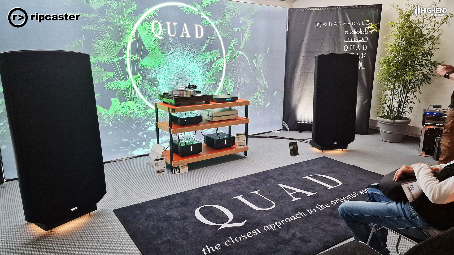 QUAD.  A pair of black floorstanding speakers either side of a HiFi unit with various pieces of HiFi kit on.