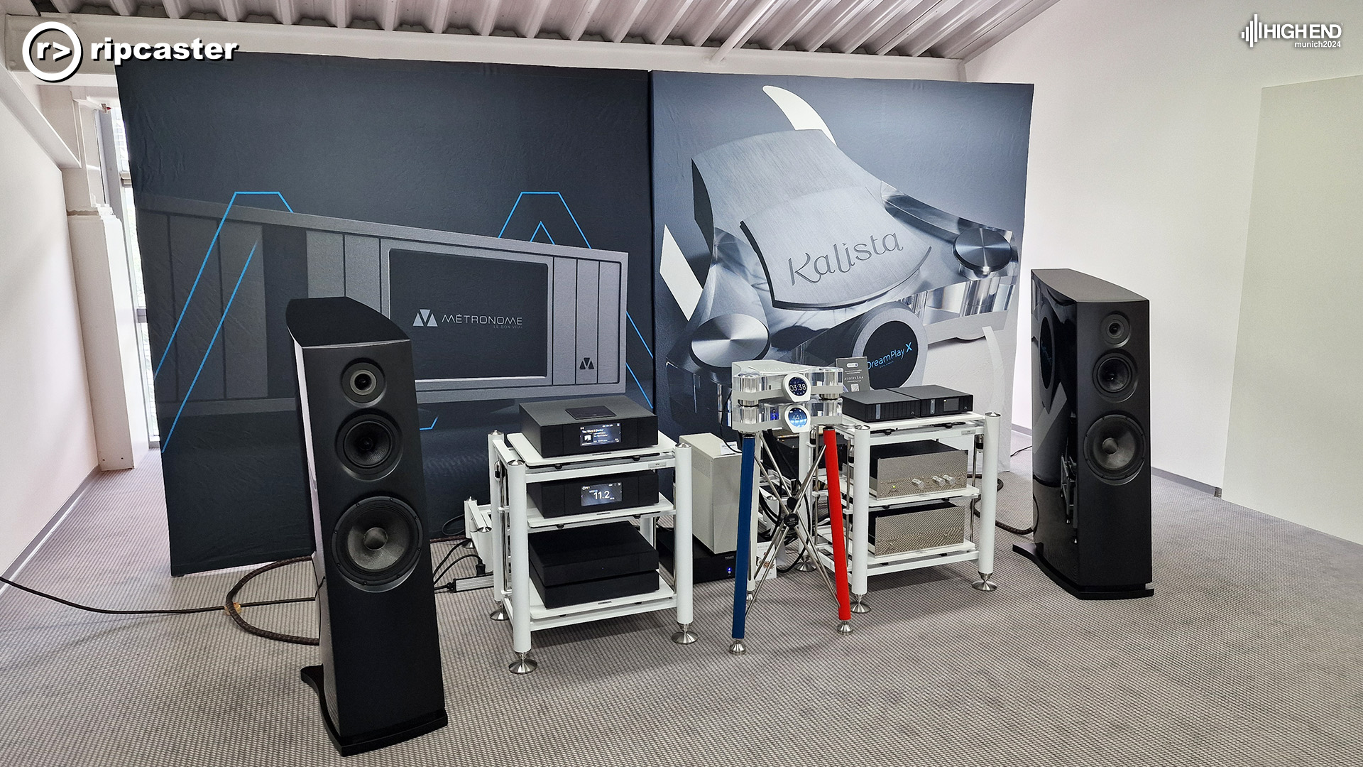 A pair of black floorstanding speakers with HiFi kit on stands between them.