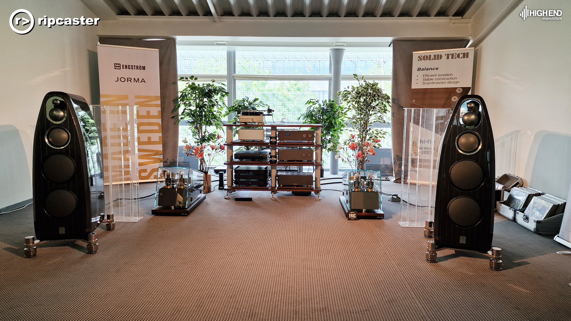 A pair of black floorstanding speakers in front of various bits of HiFi.