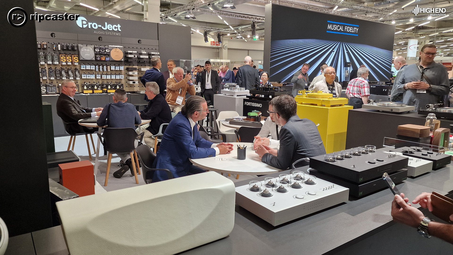 Various men standing and sitting chatting.  With HiFi equipment around them