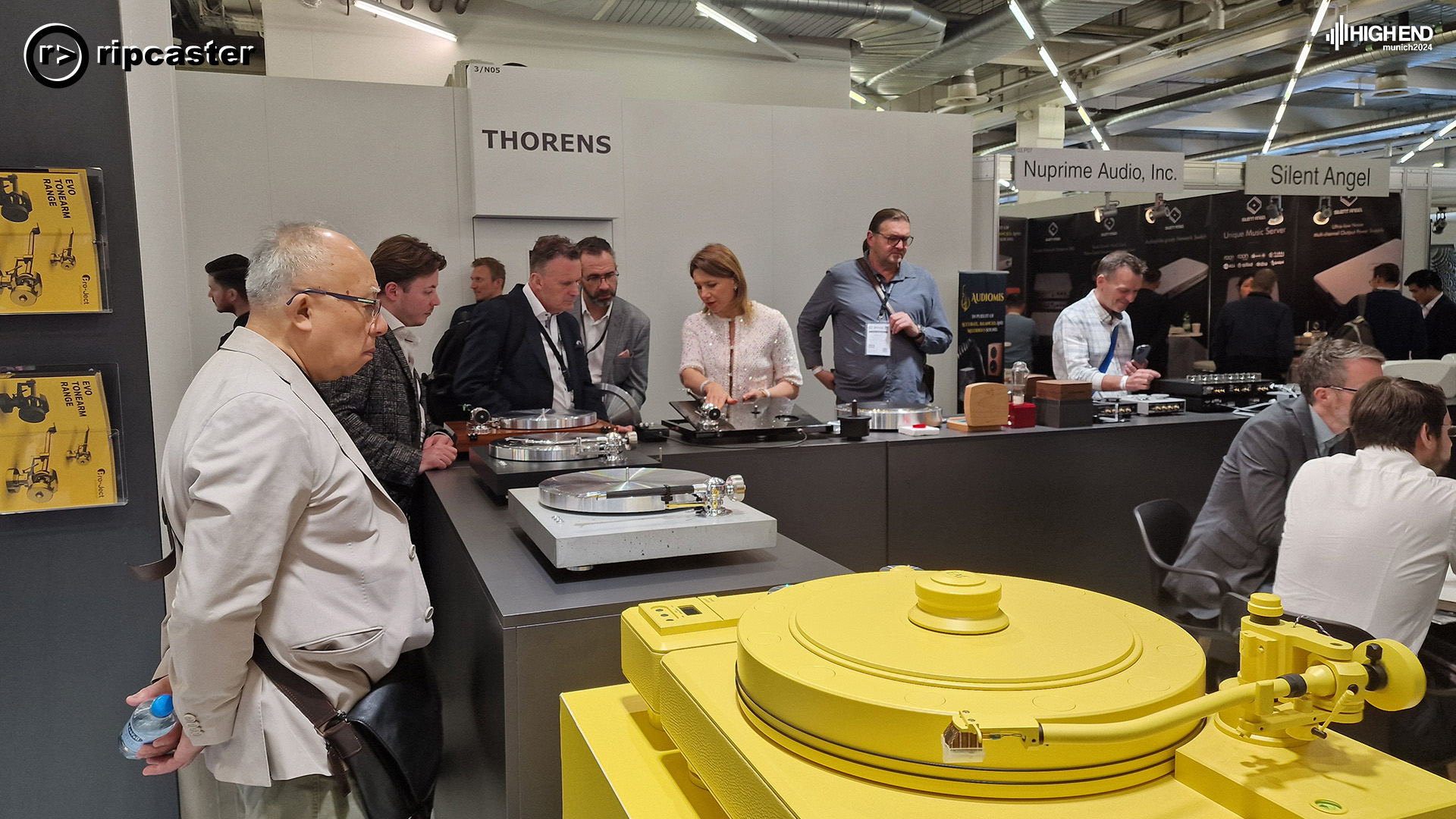 Various turntables. Thorens. with people looking at them.  One woman is in the picture.  The rest of the people are all men.