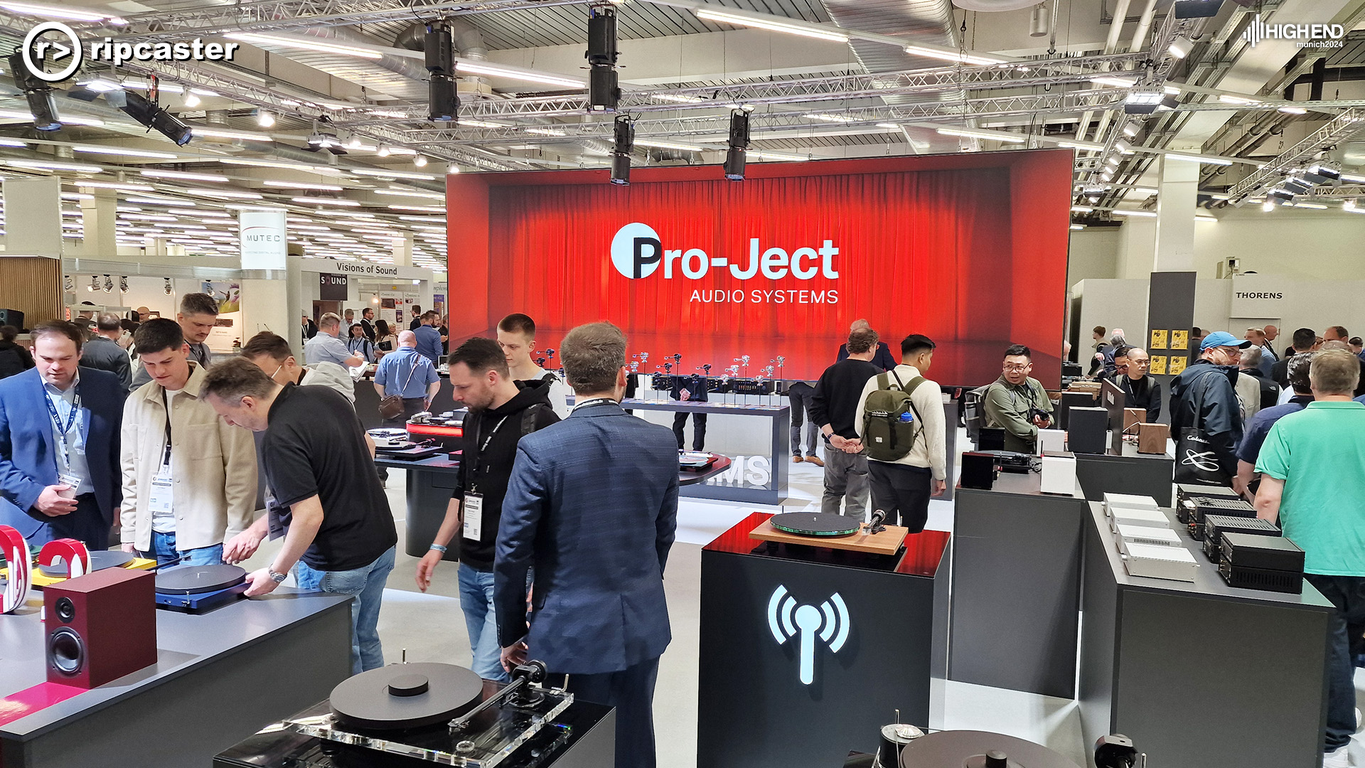 The Project Audio Systems area wide shot with lots of people (all men) looking at the turntables arranged within the space on top of black units.