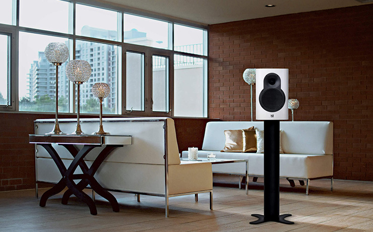 Kii Seven speaker in a living space with two cream sofas facing each other, a wooden floor and a brick wall