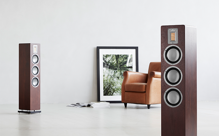 Audiovector QR5 speaker in a white space with a brown leather chair and a picture standing against the wall.