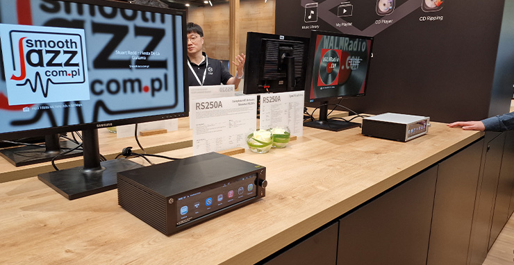 HiFi Rose RS250A on a wooden table at the Munich HiFi Show.  There are screens on the table too and a man is in the background.