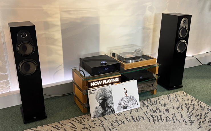 Our ripcaster Linn 150 speakers in black either side of a HiFi unit that has the Selekt DSM Classic Hub 2024 beside a Linn LP12 turntable.  There are two albums propped up against the HiFi unit