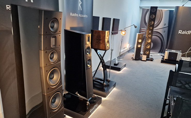 The Raidho area at the 2024 HiFi Munich show.  Three speakers lined up on the left with the RD3.8 on the furthest left. 