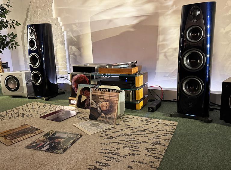 A pair of Linn 360 speakers either side of a HiFi unit with a DSM and turntable on top of it.  On the floor are various Bob Dylan albums: some propped up and some laying on the rug