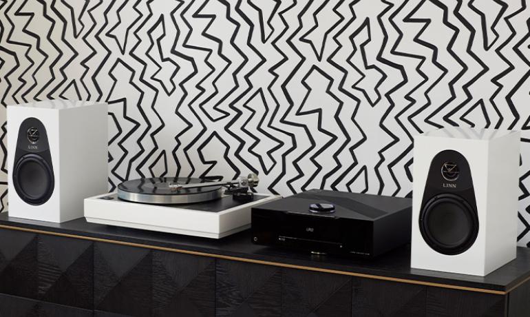 A pair of white Linn 119 speakers either side of a DSM and a turntable