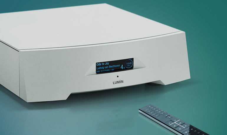 Lumin P1 Network Music Player on a green background with the remote control in front of it.