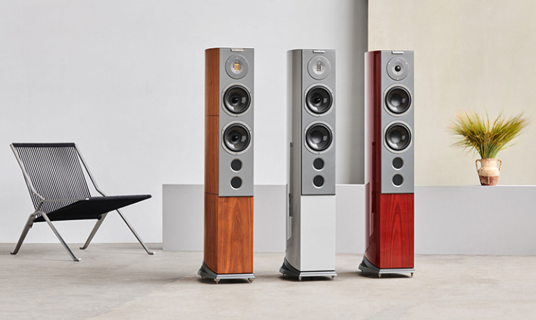The three R6 Series speakers in a large space with a chair one side and a vase the other.