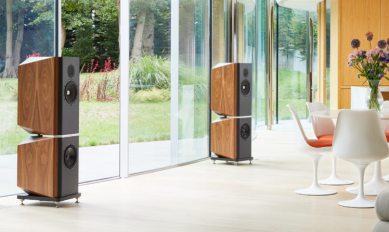 A pair of Kudos Titan 808 Speakers in a large open living area.  They are in front of a wall of large windows.