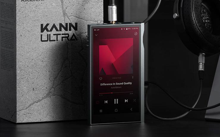 The Astell & Kern Kann Ultra standing up with headphones plugged in.  It's in front of the box which has "KANN ULTRA" in large letters on the front.