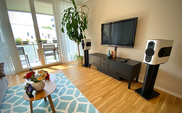 Image shows a pair of Kii Three speakers in white in a living room either side of a television.