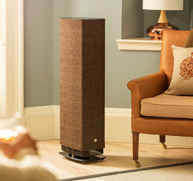 Linn Series 5 530 Exakt Active Speaker in Harris Tweed beside a chair in a well lit living room.  There's a large lamp in the background.