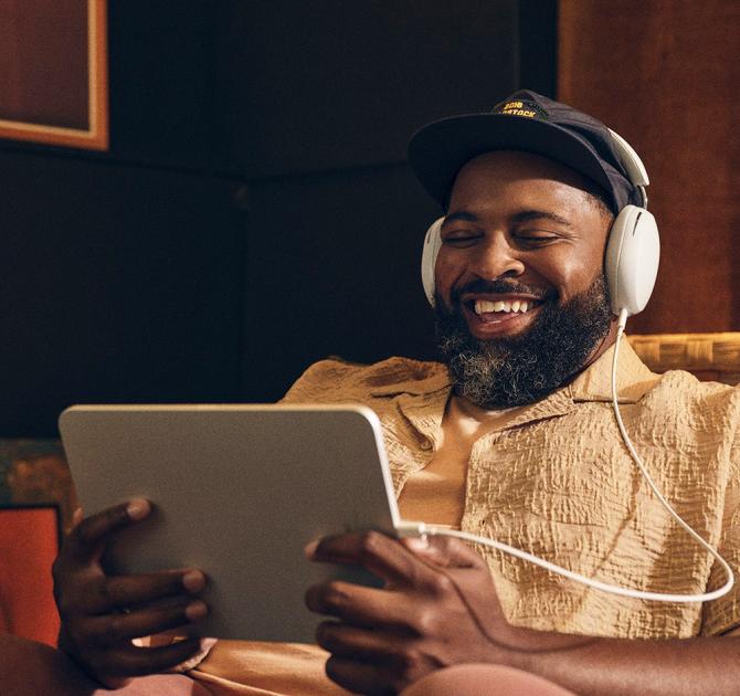 Sonos Ace Headphones in white on the head of a man.  He's holding a tablet and smiling