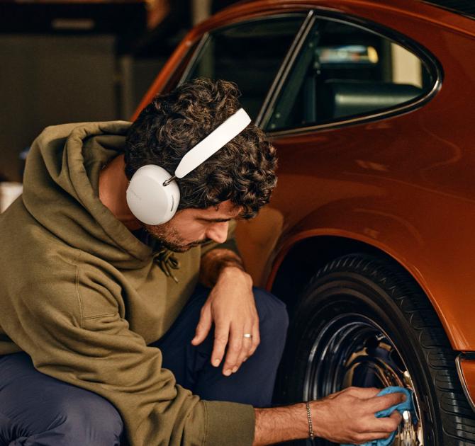 Sonos Ace Headphones in white on the head of a man working on the wheel of a car
