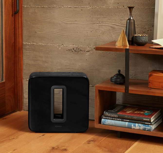 SONOS Sub in black next to a set of floor standing shelves