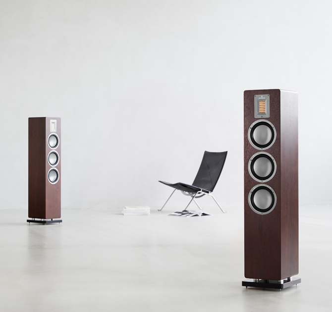 Audiovector QR5 pair in dark walnut with a chair between them.