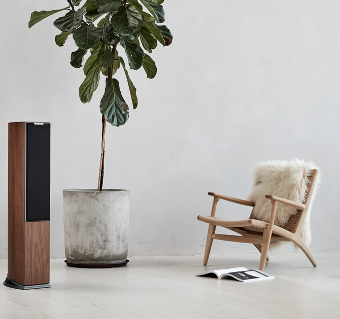 Audiovector R3 Arreté in Italian Walnut, grille on with a large houseplant and a chair