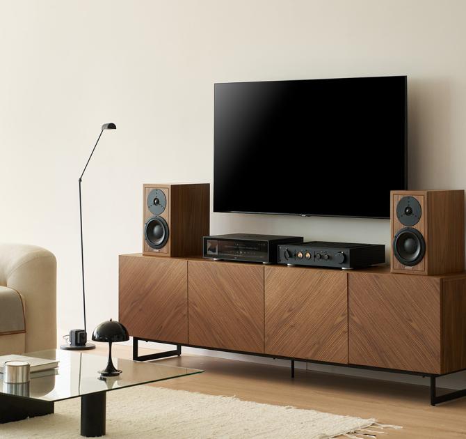 HiFi Rose RS151 Streamer/DAC on a low unit underneath a wall mounted TV.  Bookshelf speakers are either side on the unit.