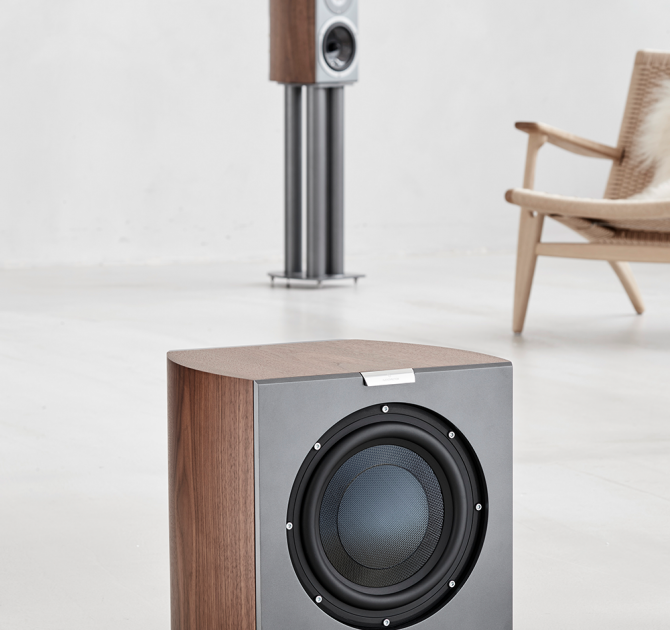 Audiovector R Sub in Italian Walnut with a chair and speaker in the background