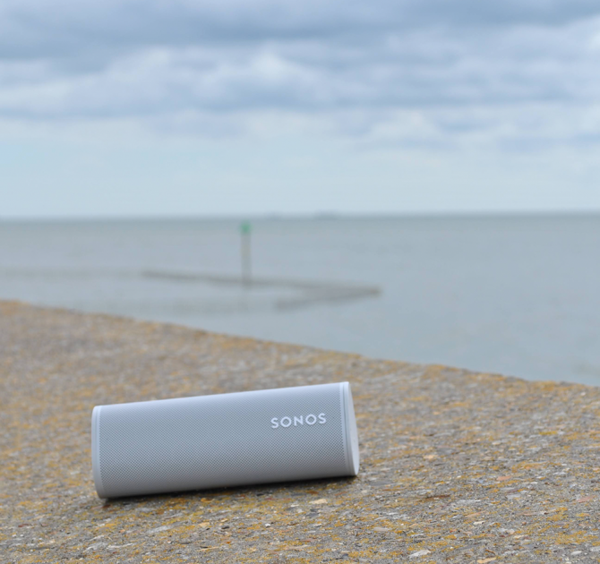 SONOS Roam in white on a sea wall with the sea in the background.