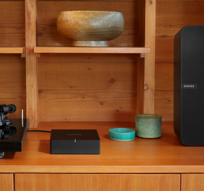SONOS Port on a wooden sideboard with a bowl on a shelf above it and a SONOS Play:5 to the right.