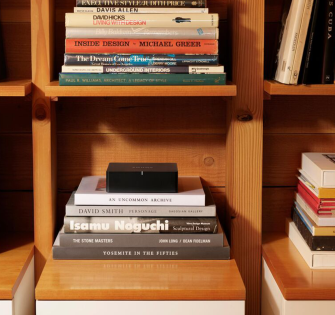 SONOS Port in a wooden modular shelving unit on top of a stack of books.