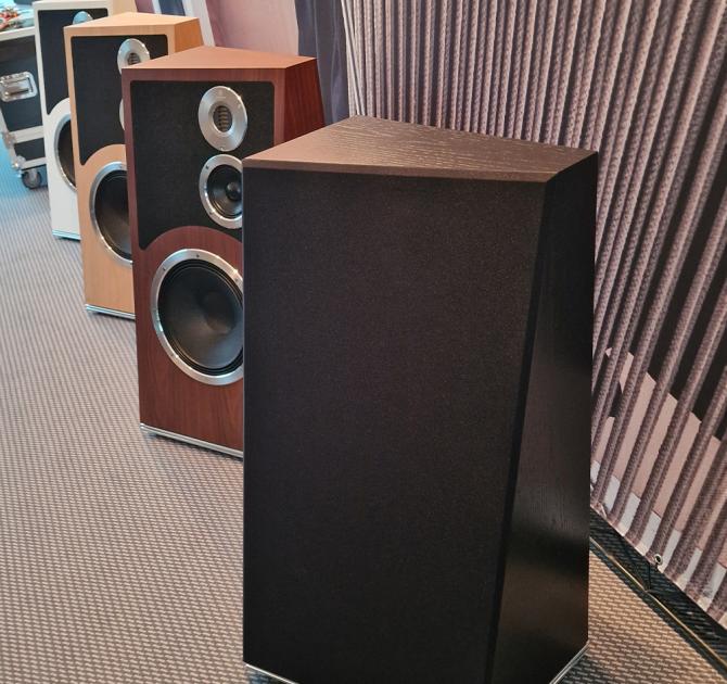 Audiovector Trapeze Ri in black with the grille in place.  there are other Trapeze speakers behind and to the left of it without Grilles on.