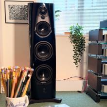 Linn 360 floor-standing speaker in Linn Heritage dark navy gloss finish, featuring multiple high-performance drivers for precise, dynamic sound. Shown in a modern listening room with a stack of hi-fi components, trailing green houseplant, and a ceramic mug filled with colourful pencils.