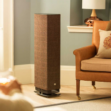 Linn Series 5 530 Exakt Active Speaker in Harris Tweed beside a chair in a well lit living room.  There's a large lamp in the background.