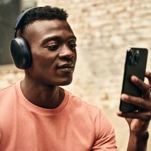Sonos Ace Headphones in black on the head of a man who is looking at his phone