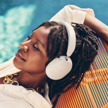Sonos Ace Headphones in white on the head of a woman who is laying beside a swimming pool