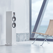 Audiovector QR3 in white silk by a window with a sea view and a chair by the speaker