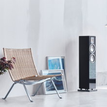 Audiovector QR3 in piano black with two pictures leaned against the wall and a chair beside the speaker.