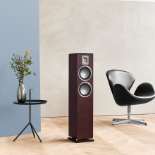 Audiovector QR3 in dark walnut with a chair beside it and a small table holding a vase of flowers the other side.