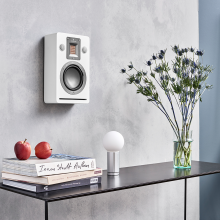 Audiovector QR Wall in white silk above a table with books, a lamp and a vase of flowers on.