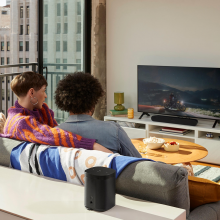 Sonos Ray Smart Soundbar in black on a tv stand with a couple in the foreground sitting on a sofa